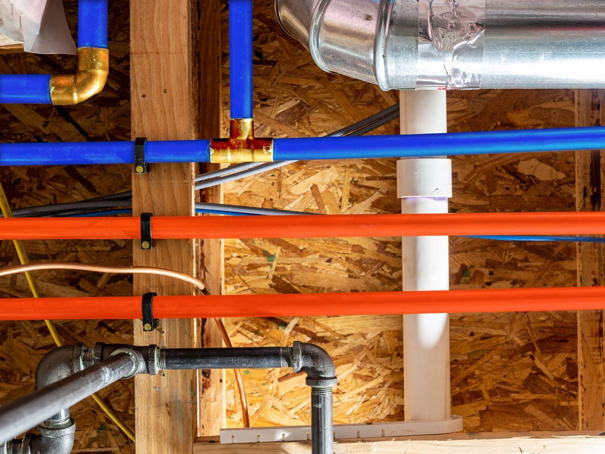 Blue and orange water supply pipes and white drain piping installed between wooden framing